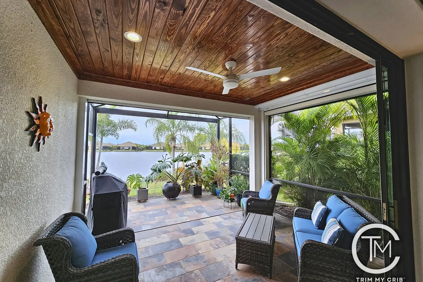 Cozy lanai seating area under a stained wood plank ceiling with a ceiling fan, opening to a tropical garden and lake