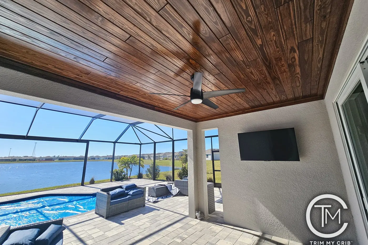 Covered lanai with a rich stained tongue-and-groove wood ceiling, a wall-mounted TV and a screened view of the lake and pool