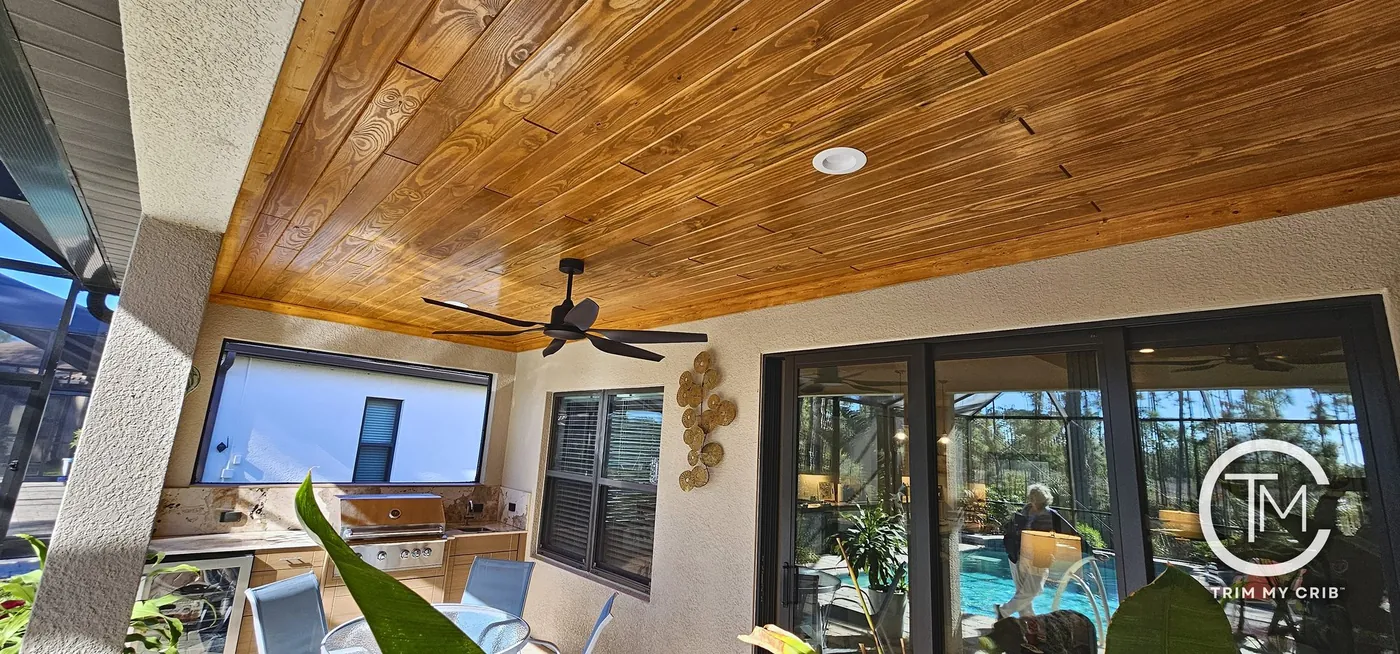 Wide panoramic view of a lanai with a warm honey wood ceiling, a ceiling fan and glass sliders to the house